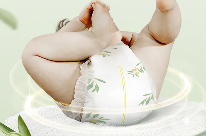 Natural baby diaper with green leaf pattern on baby’s bottom. Baby lying on back with legs up with hand over face as if gently asleep.