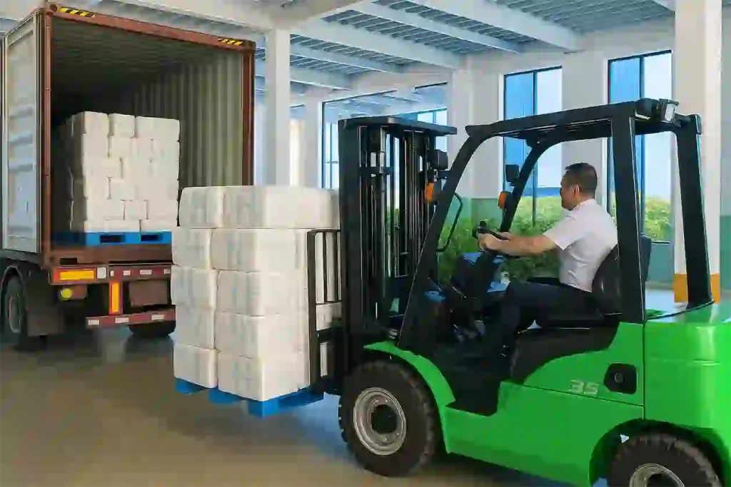 Worker operating a green forklift to load stacks of packaged products into a shipping container for delivery to international customers