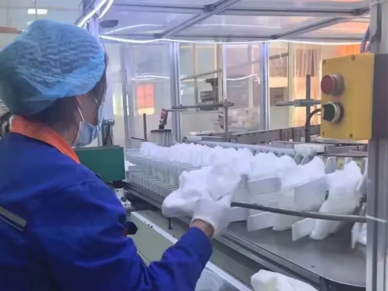 Worker operating adult diaper production line, inspecting products on conveyor.
